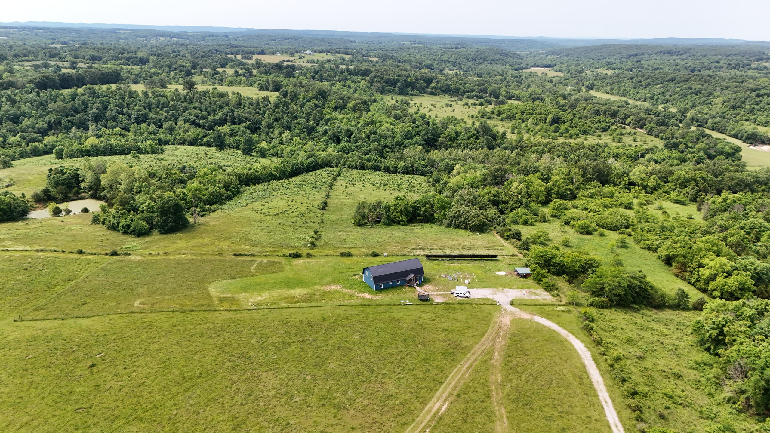Ozark hills and pasture seen from above, with a homestead at the edge of the woods